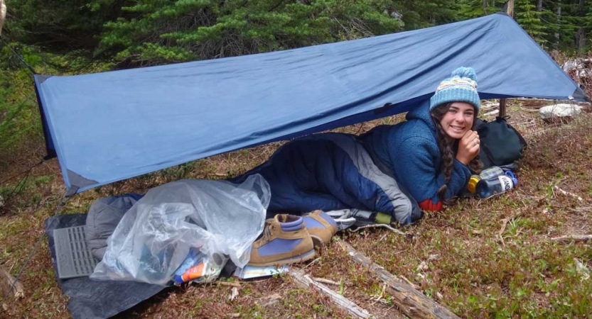 a person smiles while laying under a tarp in the woods on an outward bound expedition 